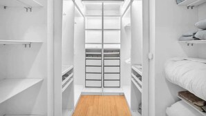 A walk-in closet with multiple shelves and drawers, a wooden floor, and a white door.
