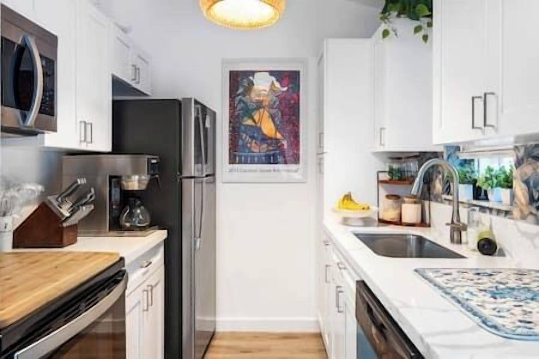 A modern kitchen with white cabinets, a stainless steel refrigerator, a coffee maker, and a sink with a blue patterned mat.