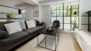 A modern living room with a grey sofa, a black coffee table, and a TV on a white stand. - w* | Radiant 2BR in Roma Norte (Ciudad de México)