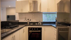Una cocina moderna con armarios blancos, una campana extractora de acero inoxidable, un horno empotrado y un refrigerador.