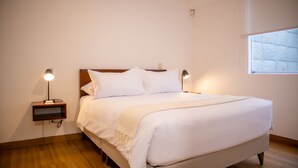 Una cama bien hecha con ropa blanca y un cabecero de madera en una habitación con suelo de madera.