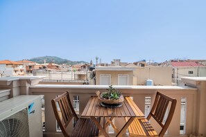 A wooden table with chairs on a balcony overlooking a cityscape with buildings and a mountain in the distance. - ExAnimo Luxury Apt 2 (Zakinthos)