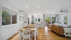Un salón amplio con mesa de comedor, muebles blancos, un sofá marrón y ventanas grandes.