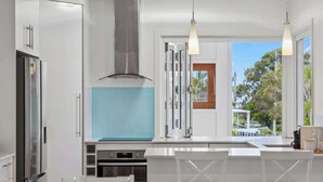 Una cocina moderna con armarios blancos, una campana extractora de acero inoxidable y vistas al exterior.