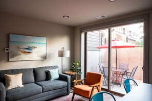 A living room with a sofa, a chair, a table, and a painting of a beach scene.