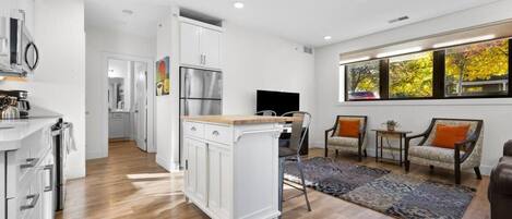 Una cocina moderna con armarios blancos, horno empotrado y comedor con mesa y sillas de madera.