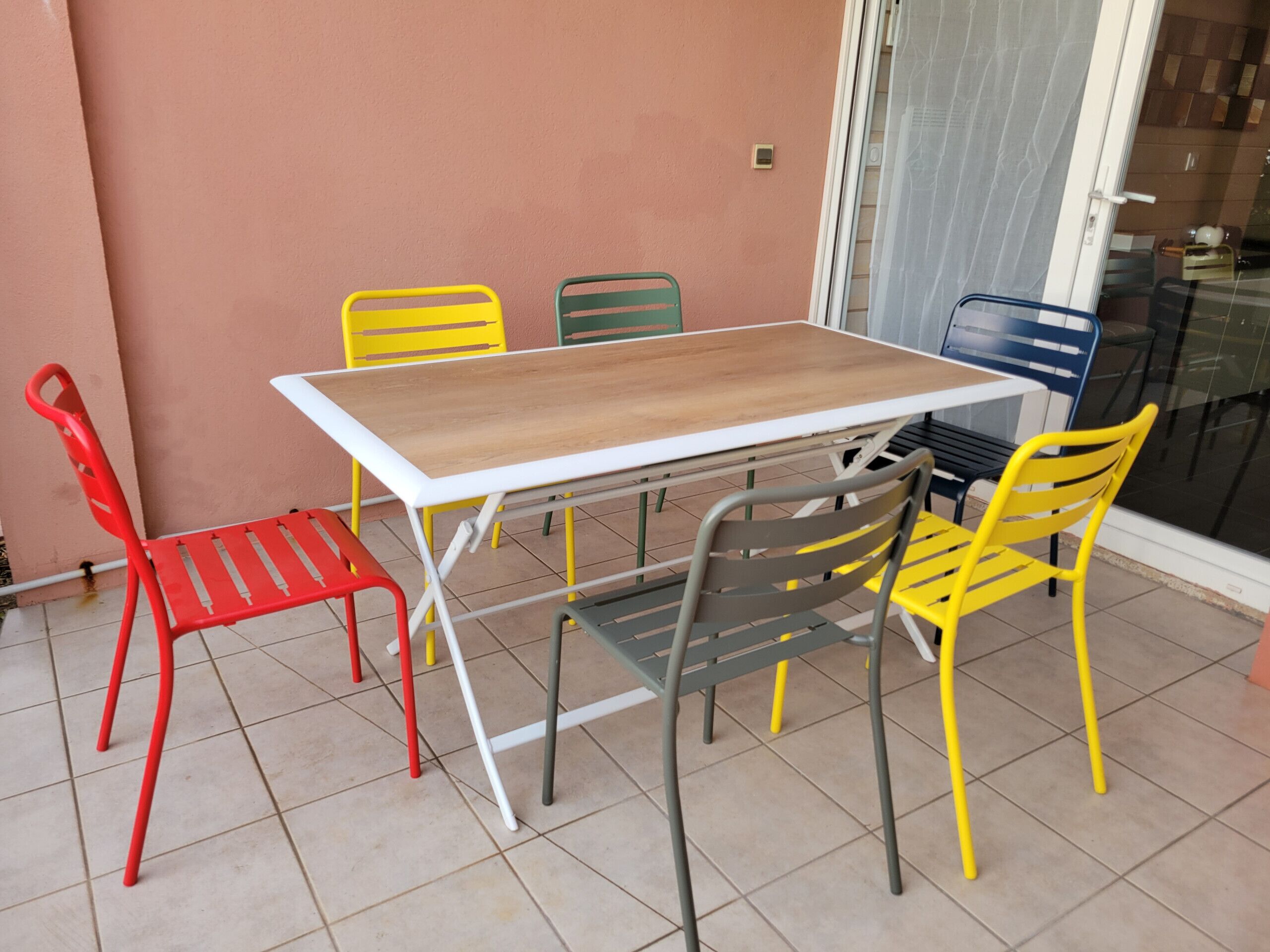 A patio with a wooden table and six chairs in various colors.
