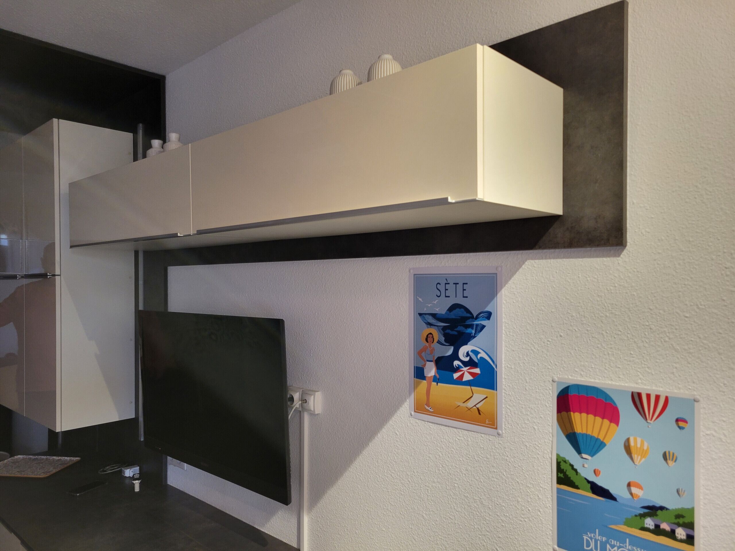 Een keuken met een ingebouwde magnetron, een zwarte oven en een wit kastje erboven. Er hangen twee posters aan de muur: één met een strandgezicht en de andere met luchtballonnen.