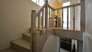 A staircase with white railings and a wooden floor, leading to a room with a bed and a window.