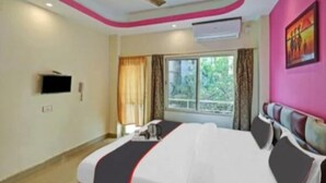 A hotel room with a large bed, a flat-screen TV, a window with curtains, and a ceiling fan. - DhamStay Hotel Shree Bhumi Near SeaBeach (Puri)