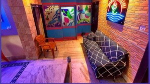 A room with a sofa, a chair, a TV, and a wall with a colorful mural. - DhamStay Hotel Shree Bhumi Near SeaBeach (Puri)