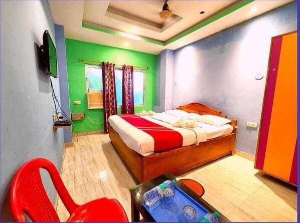A bedroom with a bed, a desk, a chair, a television, and a window with curtains.
