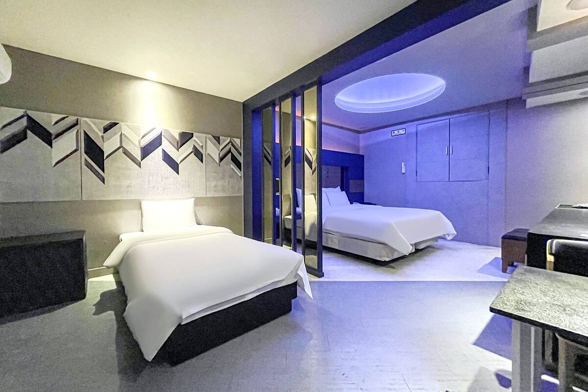 A modern hotel room with two beds, a desk, and a bathroom with a shower and toilet.