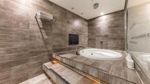 A modern bathroom with a large bathtub, wooden wall tiles, a built-in TV, and a glass shower enclosure. - HOTEL ON (Uiwang)