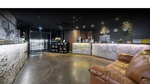 A modern reception area with a stone counter, leather seating, and a reception desk with clocks. - HOTEL ON (Uiwang)