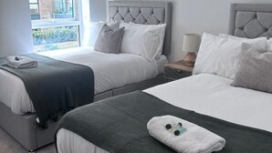 A hotel room with two beds, grey headboards, white bedding, and a window offering a view of the outside.