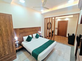 Habitación de hotel con una cama grande, cabecera de madera, ventilador de techo, mesita de noche, espejo y armario.