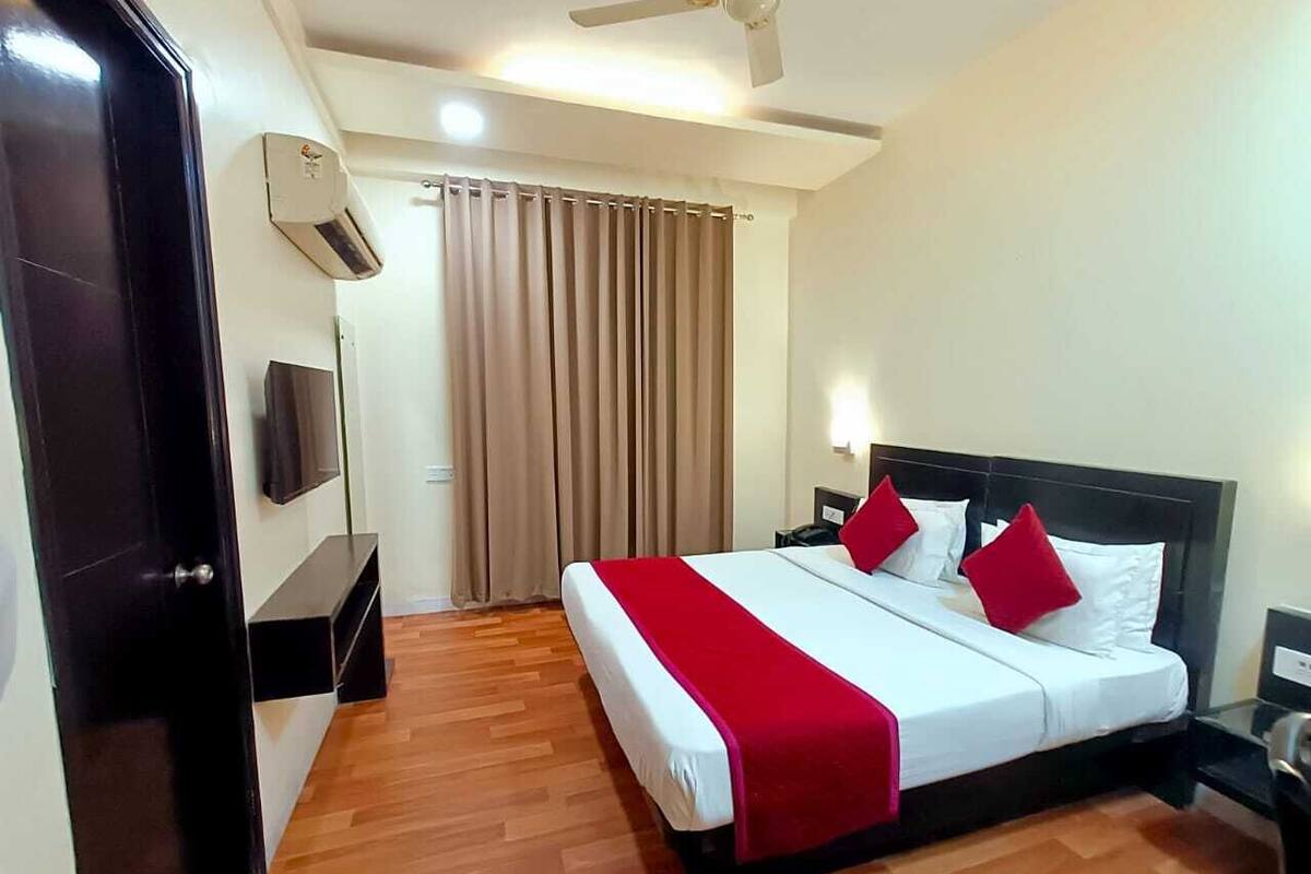 A hotel room with a bed, a TV, a ceiling fan, and a window with curtains.