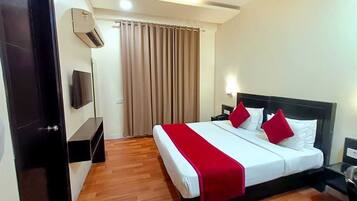 Habitación de hotel con cama, televisión, ventilador de techo y ventana con cortinas.