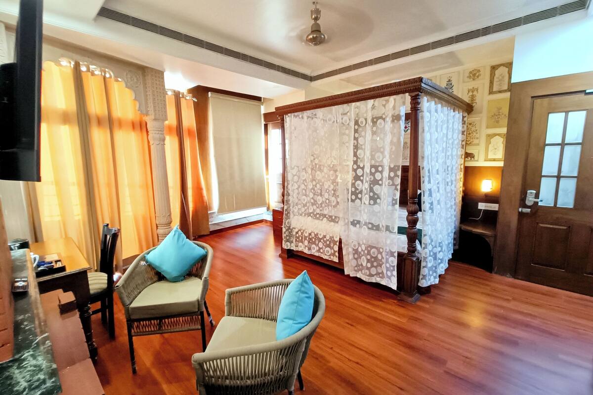 A hotel room with a wooden floor, a four-poster bed, wicker chairs, and a television.