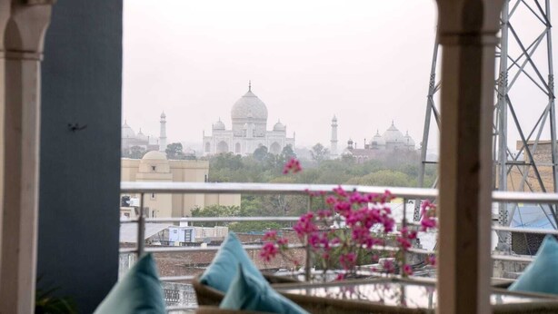 Uma varanda com cadeiras e almofadas de vime, com vista para o Taj Mahal.