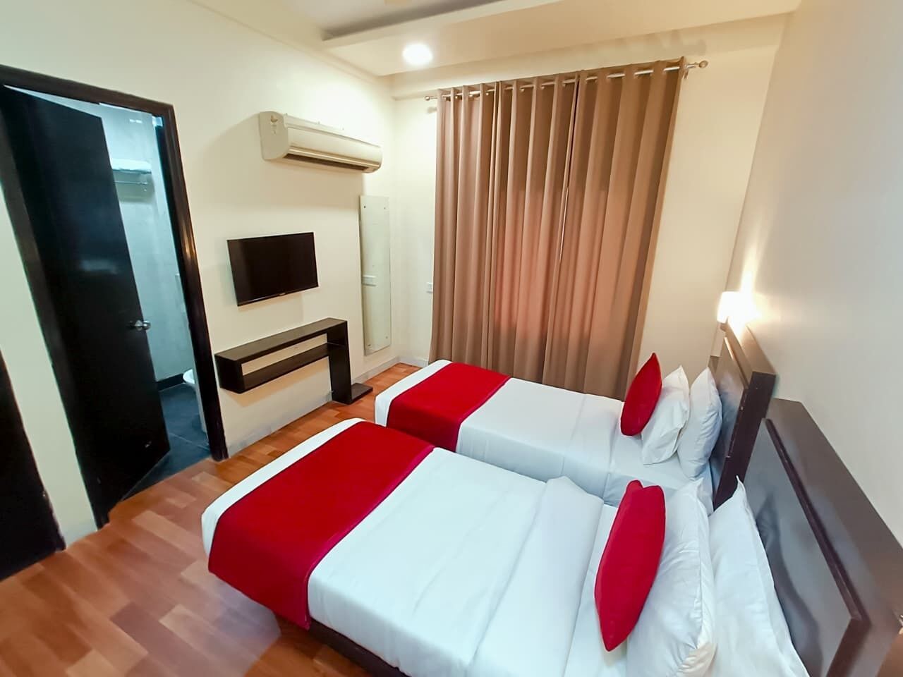 A hotel room with two beds, a TV, an air conditioning unit, and a curtain.