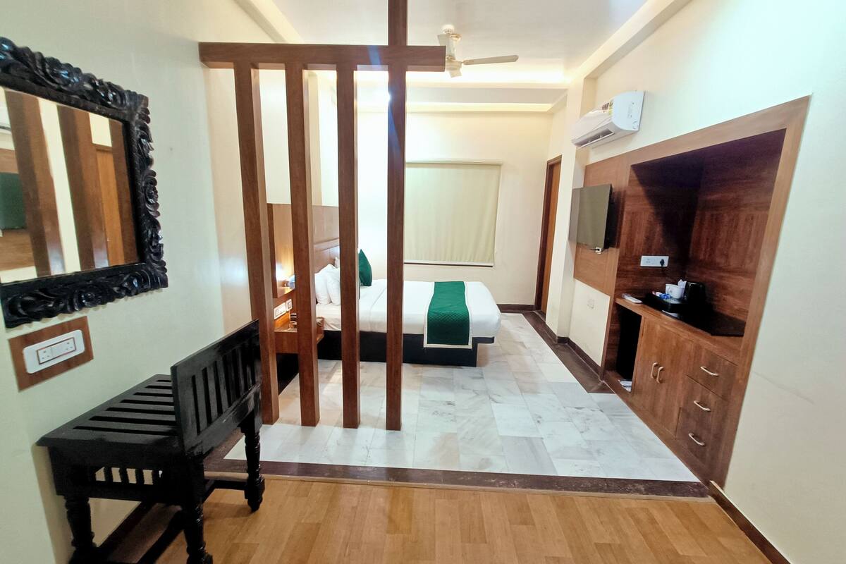 A hotel room with a bed, a wooden bench, a mirror, a wardrobe, and a ceiling fan.