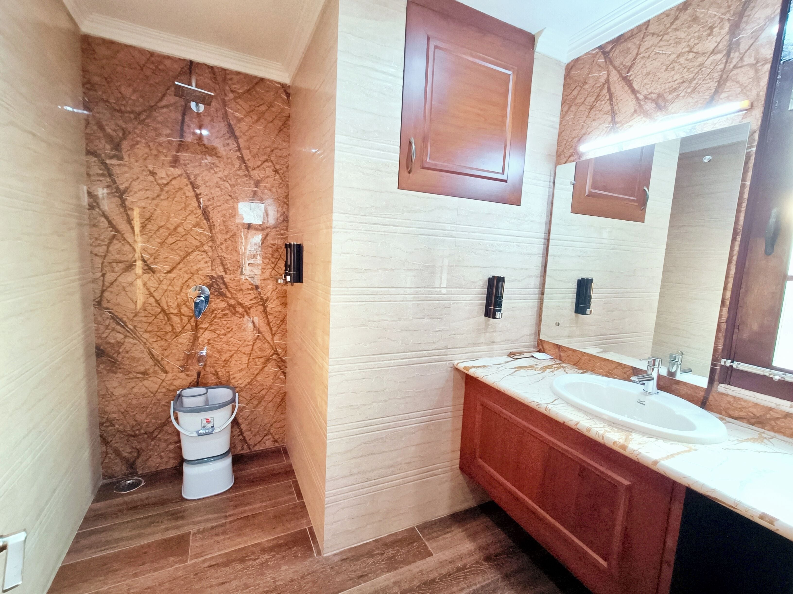 A bathroom with a marble wall, wooden vanity, and a large mirror.