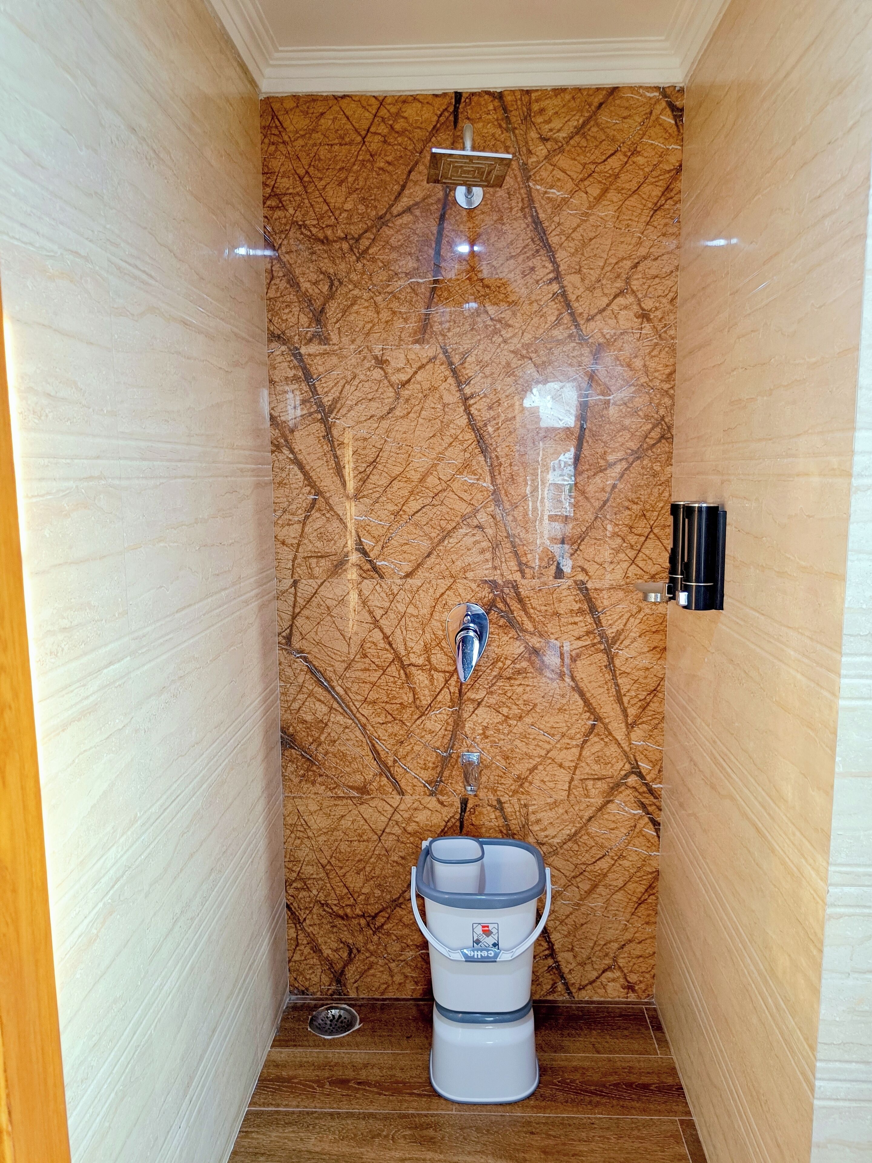 Un baño con pared de mármol, ducha, inodoro y dispensador de agua.