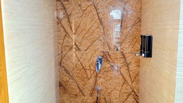 Un baño con pared de mármol, ducha, inodoro y dispensador de agua.
