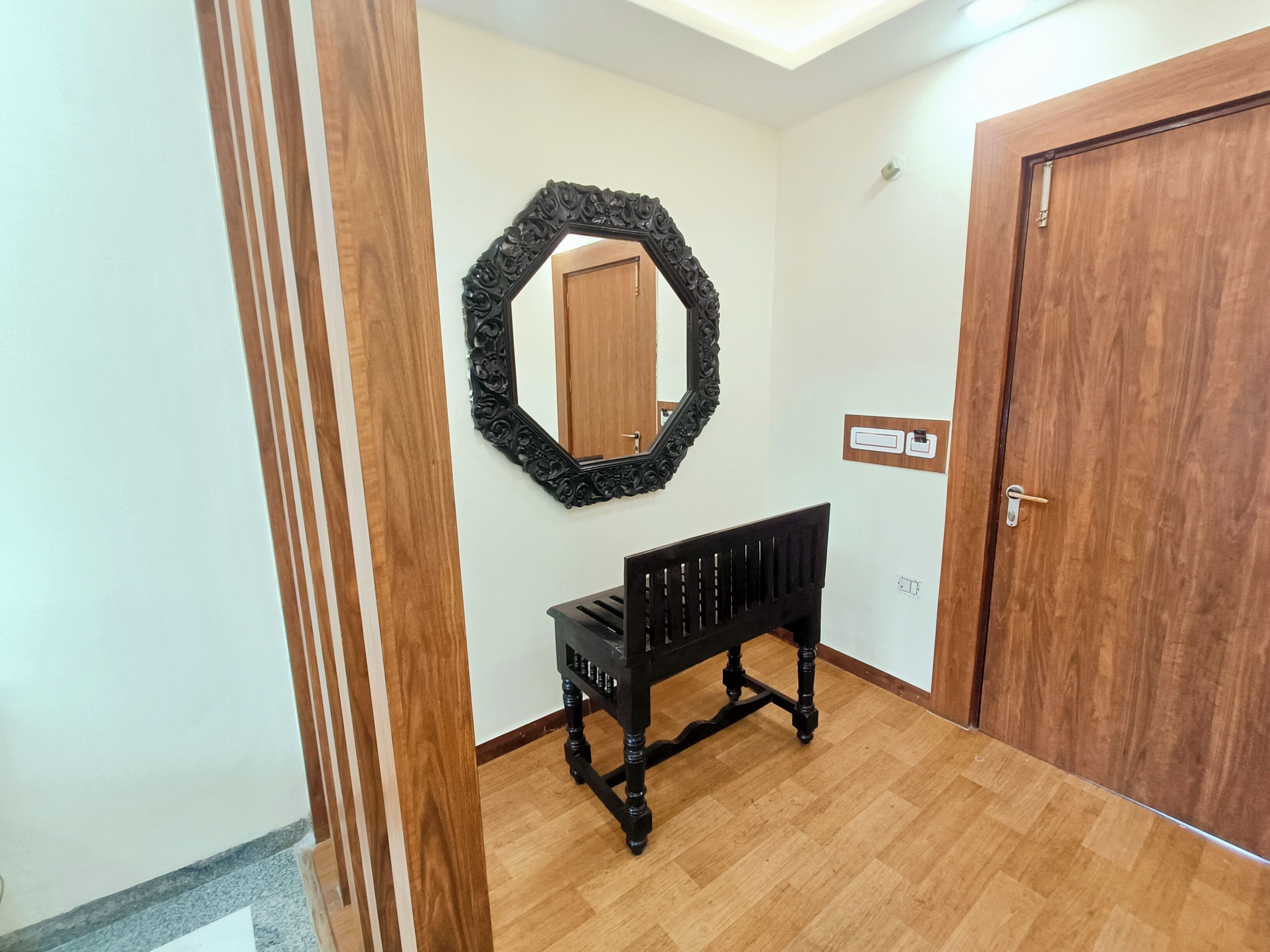 A hallway with a wooden floor, a black bench, a wooden door, and a wall-mounted mirror.