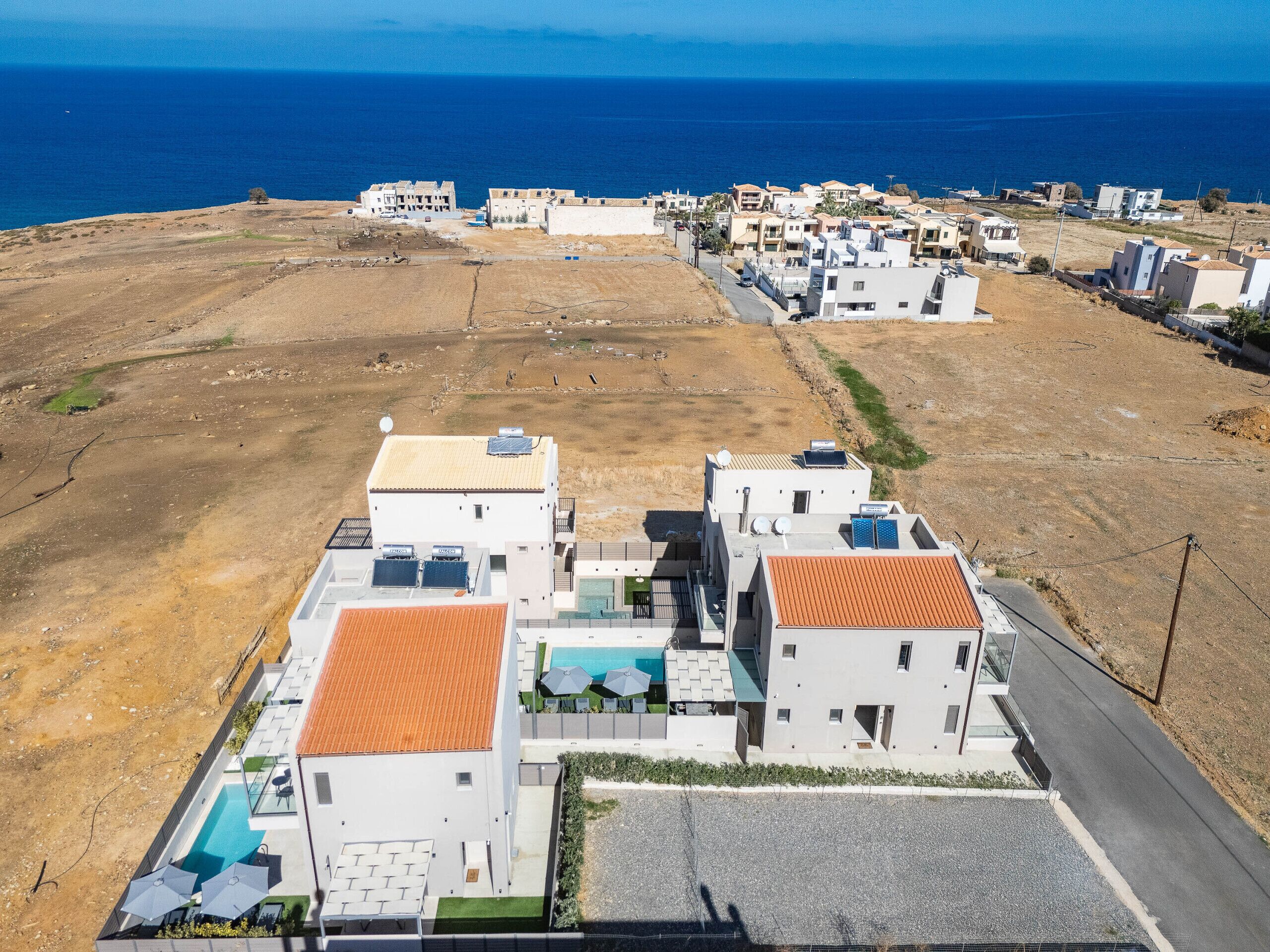 A modern residential area with a swimming pool, solar panels, and a view of the sea.