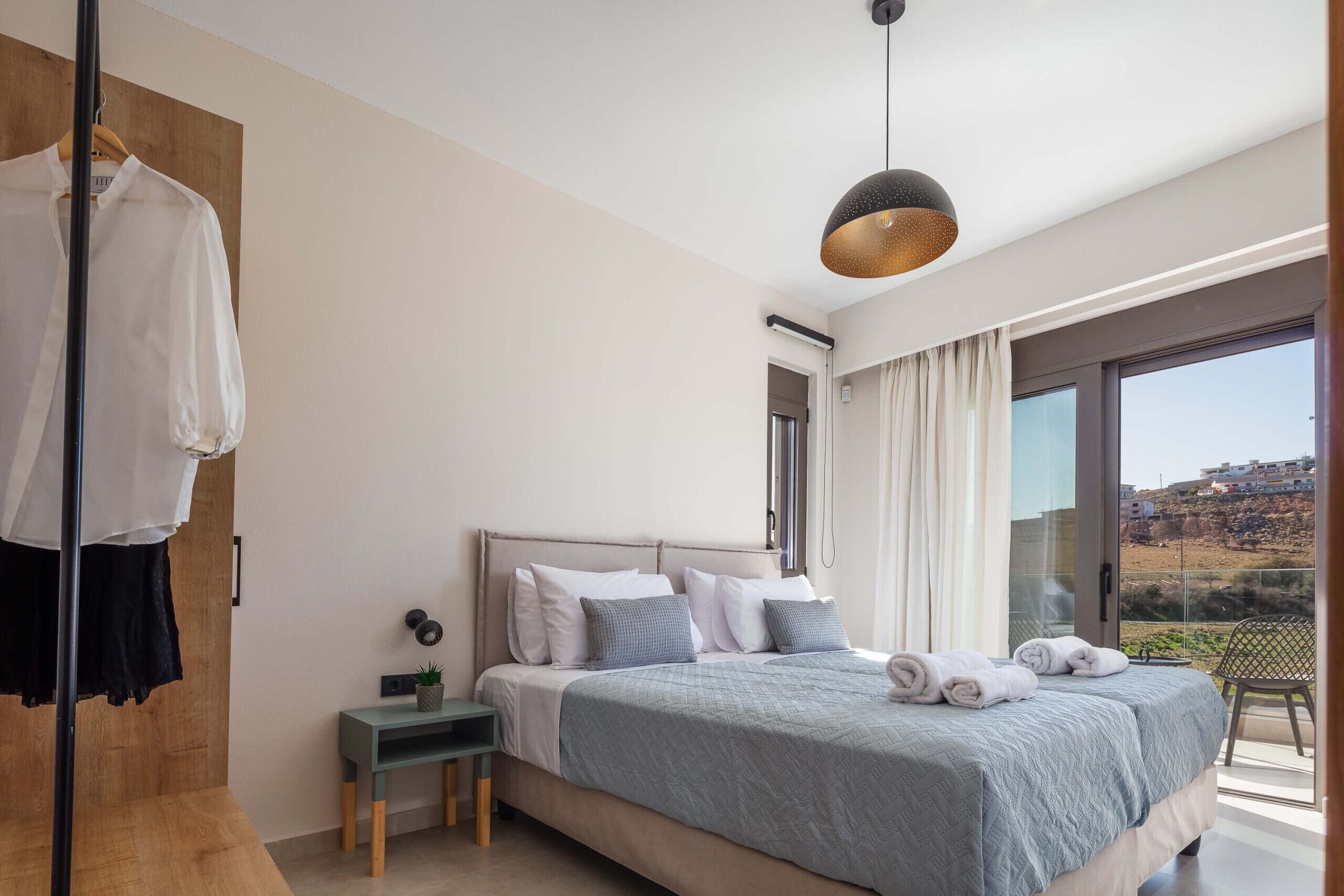 Ein modernes Schlafzimmer mit einem großen Bett, einem kleinen Nachttisch, einem Kleiderhaken und einem Balkon mit Blick.