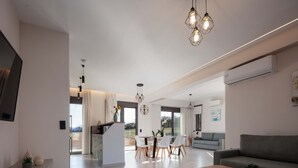 A modern living room with a sofa, a dining area with chairs, and a kitchen area with a counter. - Walking distance from the beach, villa complex with 2 pools! (Panormo)