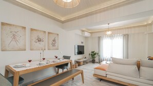 A modern living room with a dining area, a sofa, a TV, and artwork on the walls.