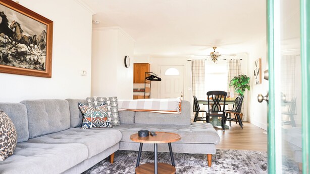 Ein Wohnzimmer mit einem grauen Ecksofa, einem runden Couchtisch und einem Gemälde von Pferden.