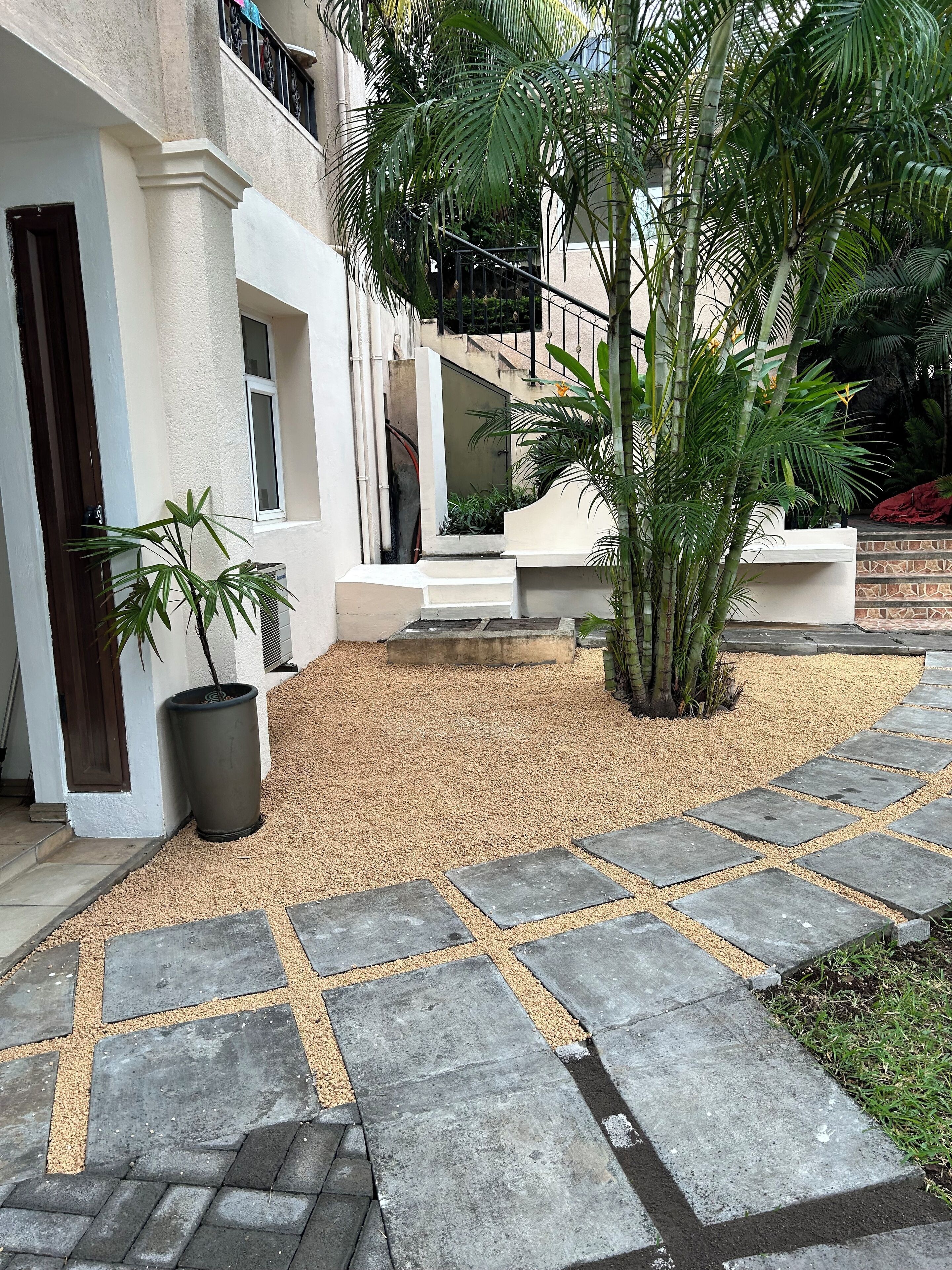 A courtyard with a gravel path, potted plants, and a building with a balcony.