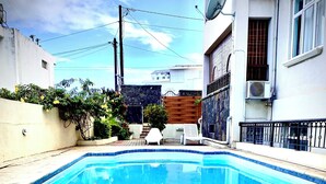 Una piscina rectangular con borde de azulejos, rodeada de un patio con suelo de piedra.