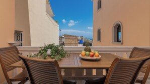A wooden table with chairs, a fruit bowl, and a potted plant on a balcony with a view of buildings and the sky. - ExAnimo Luxury Apt 5 (Zakinthos)