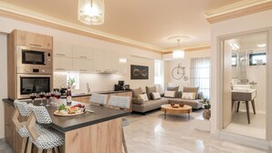 A modern kitchen with built-in appliances, a dining area with bar stools, a living room with a sofa and coffee table, and a bathroom with a mirror and sink. - ExAnimo Luxury Apt 5 (Zakinthos)