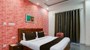 Une chambre d’hôtel avec un mur décoré d’un motif en briques, un lit en bois avec une literie blanche et noire, une table de chevet, une chaise rouge et une fenêtre avec des rideaux foncés.