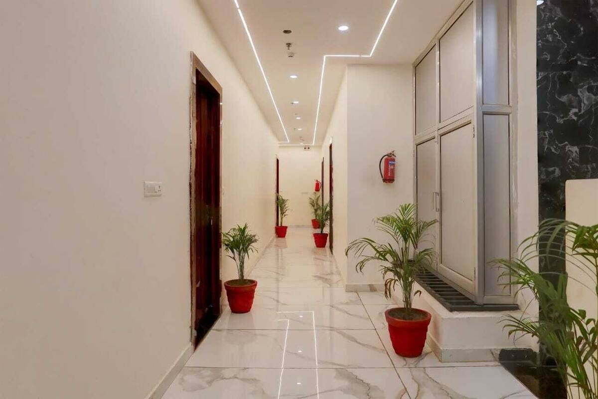 A hallway with a marble floor, red potted plants, and a fire extinguisher on the wall.