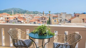 A balcony with wicker chairs and a table, overlooking a coastal town with buildings and a hill in the background. - ExAnimo Luxury Apt 6 (Zakinthos)