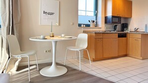A modern kitchen with white chairs, a round table, wooden cabinets, a microwave, and a coffee maker. - Vacation apartment 3 "Hygge" Rügen, Baltic Sea, Seedorf am Neuensiener See (Sellin OT Seedorf)