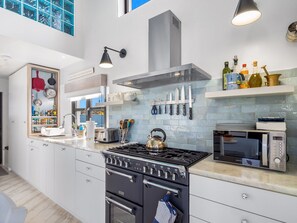 A modern kitchen with a built-in oven, microwave, and a kettle on the stove. - Ocean Mist Cottage (Carna)