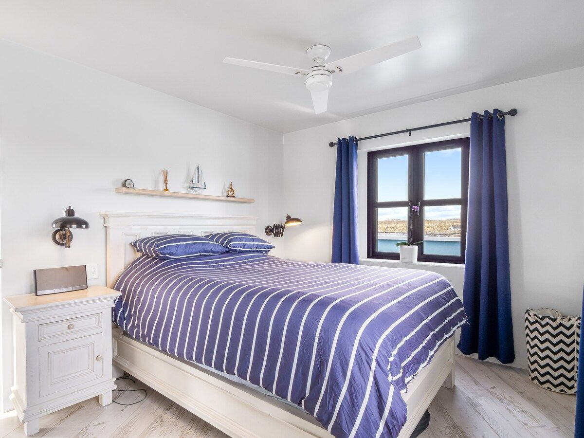 Un dormitorio con cama, mesita de noche, lámpara y ventana con cortinas.