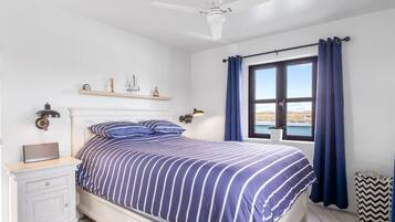 Un dormitorio con cama, mesita de noche, lámpara y ventana con cortinas.