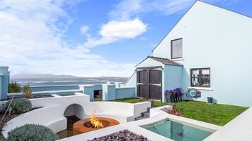 Una casa moderna con piscina, un brasero y vistas al océano.