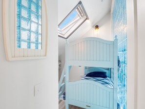 A bunk bed with a skylight above, a white wall, and a window with a blue pattern. - Ocean Mist Cottage (Carna)