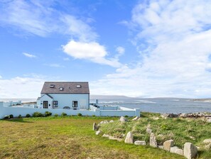 A coastal house with a view of the sea, a grassy area in the foreground, and a clear sky. - Ocean Mist Cottage (Carna)